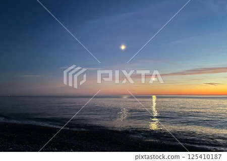 moon and the light of an airplane at night over the sea at sunset. Two moon trails on the water. 125410187