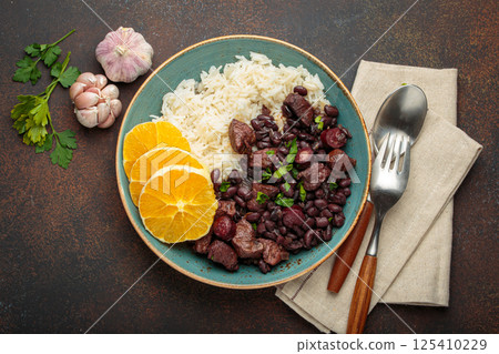 Feijoada, traditional brazilian stew with black beans, rice, and orange slices, in plate on rustic table top view 125410229