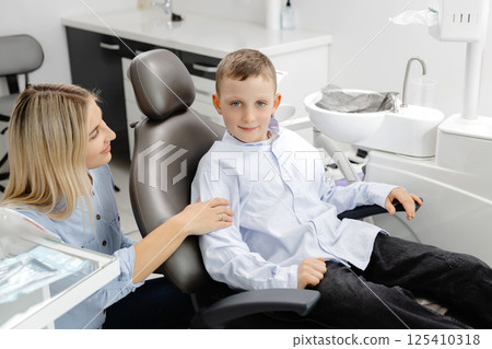Friendly dentist comforting young boy sitting on dentist chair 125410318