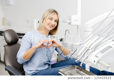 Patient showing heart shape with hands sitting in dentist chair 125410325