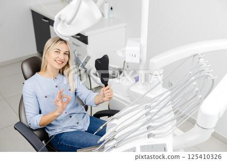 Patient showing ok sign while holding dental mirror at clinic Patient showing ok sign while holding dental mirror at clinic 125410326