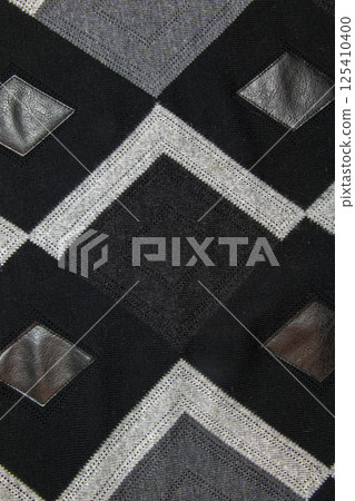 Detailed inserts in black genuine leather on a knitted woolen background with an abstract pattern. Abstract fabric texture. 125410400