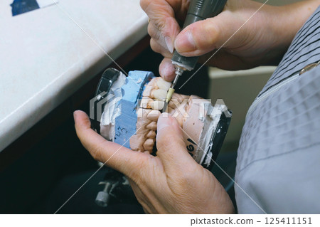 Crafting precise dentures through careful grinding by skilled dental technician 125411151