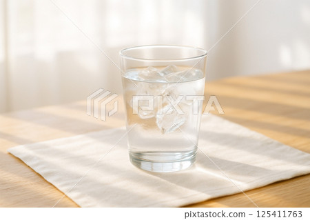A glass of ice water and a wooden table in the sunlight 125411763