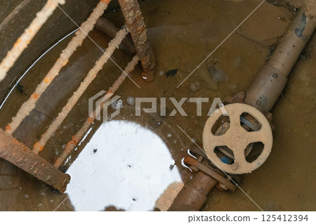 Rusty ladder leading to flooded valve in concrete chamber Rusty ladder leading to flooded valve in concrete chamber 125412394