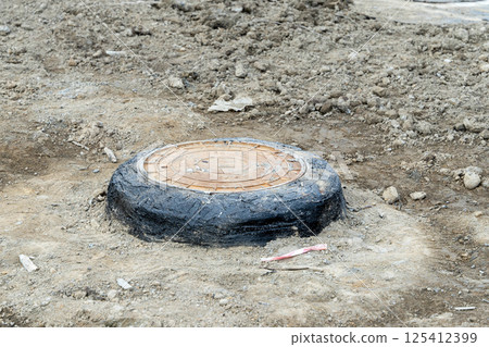 Rusty manhole cover emerging from asphalt on construction site Rusty manhole cover emerging from asphalt on construction site 125412399