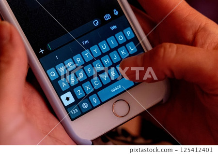 Close up of hands typing on smartphone keyboard in dark environment Close up of hands typing on smartphone keyboard in dark environment 125412401