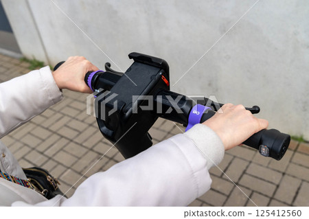 Woman riding electric scooter in urban setting holding handlebars with go sign 125412560