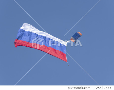 ZHUKOVSKY, RUSSIA - SEPTEMBER 01, 2021: Parachutist with a huge Russian flag in the sky ZHUKOVSKY, RUSSIA - SEPTEMBER 01, 2021: Parachutist with a huge Russian flag in the sky 125412653