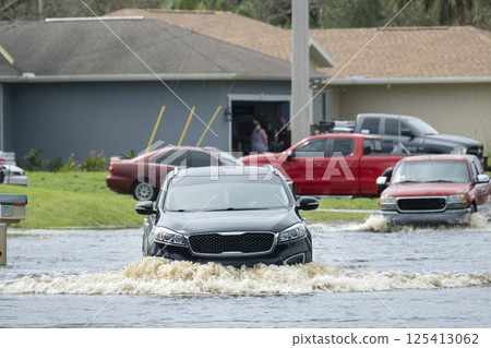 Hurricane flooded street with moving cars in surrounded with water Florida residential area. Consequences of natural disaster 125413062