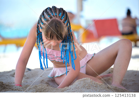 Happy child girl in swimsuit playing with sand under umbrella shadow during summer tropical vacations 125413138