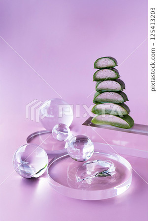 A modern setup showcases aloe slices stacked elegantly alongside serum droplets and glass orbs. A modern setup showcases aloe slices stacked elegantly alongside serum droplets and glass orbs. 125413203