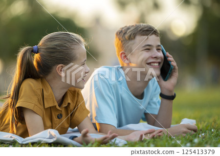 Happy teenagers talking on cellphone outdoors sitting in summer park 125413379