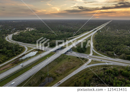 Elevated view of freeway exit junction over road lanes with fast moving traffic cars and trucks at sunrise. Interstate transportation infrastructure in USA 125413431