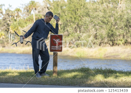 Drone operator is disappointed because he isn't allowed to fly his quadcopter in national park no drone area. Man is unable to use his UAV near restriction notice sign. Airspace use regulations Drone operator is disappointed because he isn't allowed to fly his quadcopter in national park no drone area. Man is unable to use his UAV near restriction notice sign. Airspace use regulations 125413439