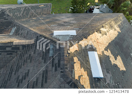 Consequences of natural disaster. Damaged house roof with missing shingles after hurricane in Florida 125413478