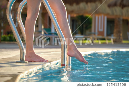 Closeup of woman legs entering swimming pool water in summer resort. Tropical vacation concept Closeup of woman legs entering swimming pool water in summer resort. Tropical vacation concept 125413506