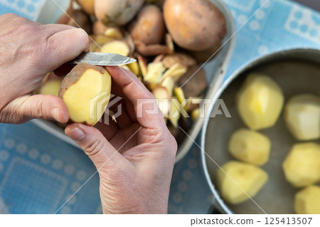 Closeup of woman hands peeling potatoes with a kitchen knife. Closeup of woman hands peeling potatoes with a kitchen knife. 125413507