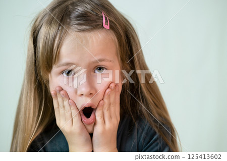 Close-up portrait of little child girl with long hair covering her mouth with hands. 125413602