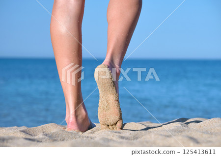 Close up of female feet walking barefoot on white grainy sand of golden beach on blue ocean water background Close up of female feet walking barefoot on white grainy sand of golden beach on blue ocean water background 125413611