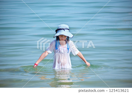 Child girl in wet white dress and big hat standing in ocean water enjoying summer vacations Child girl in wet white dress and big hat standing in ocean water enjoying summer vacations 125413621