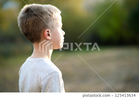 Child boy standing outdoors on summer sunny day enjoying warm weather outside. Rest and wellness concept. Child boy standing outdoors on summer sunny day enjoying warm weather outside. Rest and wellness concept. 125413634