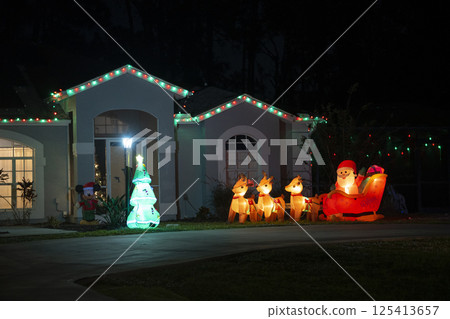 Brightly illuminated Christmas decorations on front yard of Florida family home. Outside decor for winter holidays 125413657