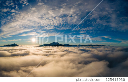 Aerial view of vibrant sunrise over white dense fog with distant dark Carpathian mountains on horizon. 125413930