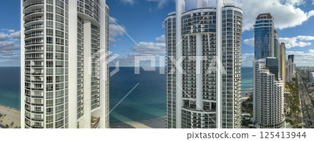 Aerial view of Sunny Isles Beach city with luxurious highrise hotels and condos on Atlantic ocean shore. American tourism infrastructure in southern Florida Aerial view of Sunny Isles Beach city with luxurious highrise hotels and condos on Atlantic ocean shore. American tourism infrastructure in southern Florida 125413944