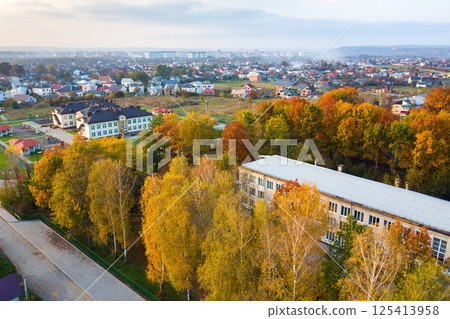 Aerial view of school, college or kindergarten building with big yard among autumn trees on rural landscape background Aerial view of school, college or kindergarten building with big yard among autumn trees on rural landscape background 125413958