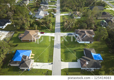 Aerial view of damaged in hurricane Ian houses roofs covered with blue protective tarp against rain water leaking until replacement of asphalt shingles Aerial view of damaged in hurricane Ian houses roofs covered with blue protective tarp against rain water leaking until replacement of asphalt shingles 125414083