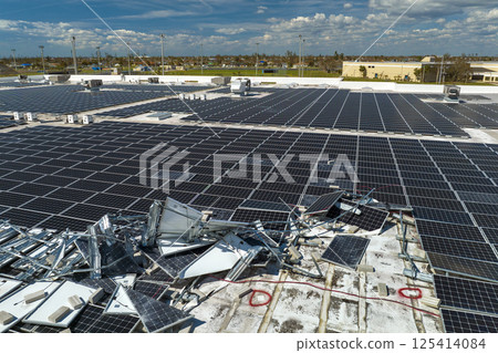 Aerial view of damaged by hurricane wind photovoltaic solar panels mounted on industrial building roof for producing green ecological electricity. Consequences of natural disaster 125414084