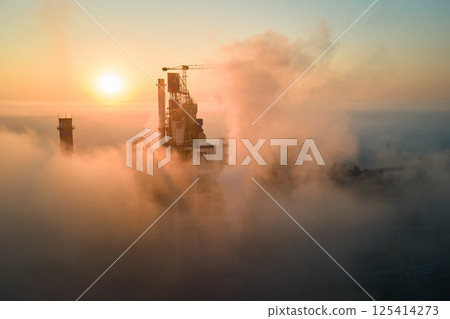 Aerial view of cement factory with high concrete plant structure and tower crane at industrial manufacturing site on foggy evening. Production and global industry concept. 125414273