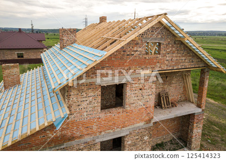 Aerial view of a brick house with wooden roof frame under construction. 125414323