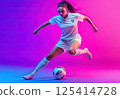 A young woman is kicking a soccer ball on a colorful background 125414728