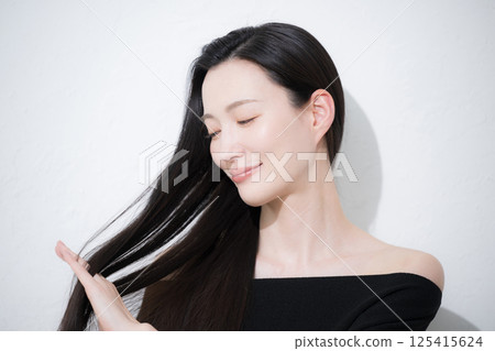 Close-up of a profile of a beautiful young woman touching her long black hair, a beauty image of her lustrous, natural skin Close-up of a profile of a beautiful young woman touching her long black hair, a beauty image of her lustrous, natural skin 125415624