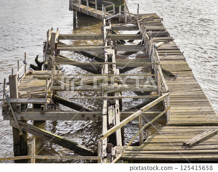 A broken of wooden supports of old timber jetty next to Swing bridge or Swing span bridge. 125415658