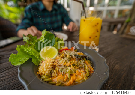 Person enjoying seafood pasta and green salad with a lime wedge on a casual restaurant table, featuring a refreshing passion fruit juice and highlighting healthy Mediterranean dining lifestyle. Person enjoying seafood pasta and green salad with a lime wedge on a casual restaurant table, featuring a refreshing passion fruit juice and highlighting healthy Mediterranean dining lifestyle. 125416433