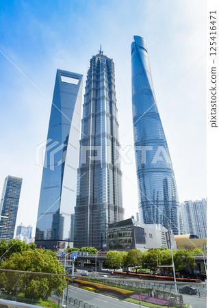 Shanghai, China - 1 April 2025: Lujiazui's iconic skyline: Shanghai Tower, Jin Mao Tower, and Shanghai World Financial Center, framed by greenery and urban infrastructure under blue skies 125416471