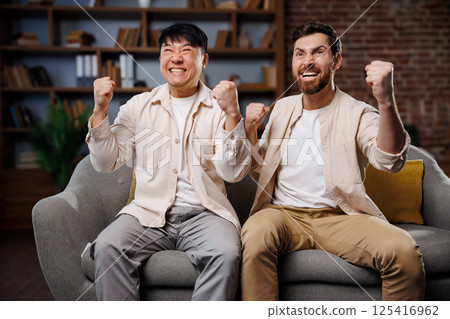 fans watching game, celebrating victory, Excited friends watching TV, Friends express their enthusiasm and joy while watching a sports event from a comfortable couch in a cozy living room. Their 125416962