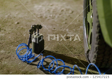 A tire repair tool rests beside a flat tire on a dirt surface. Blue air hose sprawls across the ground, indicating ongoing work in a low-light environment at night. A tire repair tool rests beside a flat tire on a dirt surface. Blue air hose sprawls across the ground, indicating ongoing work in a low-light environment at night. 125417223
