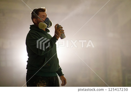 An artist wearing a mask carefully applies spray paint to a blank wall in a dimly lit industrial space. The atmosphere is artistic and focused, capturing the essence of creativity in action. An artist wearing a mask carefully applies spray paint to a blank wall in a dimly lit industrial space. The atmosphere is artistic and focused, capturing the essence of creativity in action. 125417230