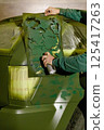 A person applies a green camouflage design on a vehicle using a spray can and a stencil. The workshop setting shows preparations for painting, highlighting creativity and craftsmanship. 125417263