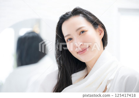 A woman looking at the camera while towel drying her hair after a bath A woman looking at the camera while towel drying her hair after a bath 125417418