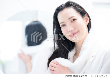A woman towel-drying her hair after a bath 125417424