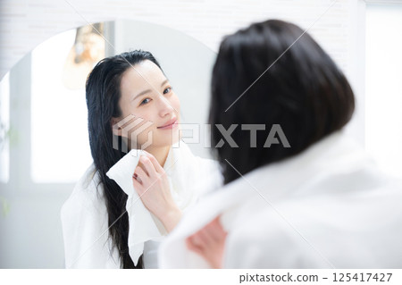 A woman towel-drying her hair after a bath 125417427