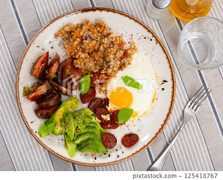 Homemade breakfast served with buckwheat, sun-dried tomatoes, avocado, fried eggs and hunting sausages Homemade breakfast served with buckwheat, sun-dried tomatoes, avocado, fried eggs and hunting sausages 125418767