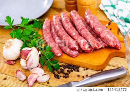 Raw sausages longaniza with greens, garlic and spices on wooden cutting board Raw sausages longaniza with greens, garlic and spices on wooden cutting board 125418772
