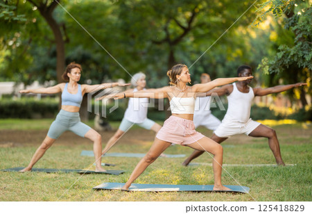Girl performing Warrior Pose during group yoga in summer park 125418829