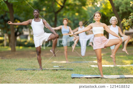 Girl performing one leg balancing pose during group yoga in park Girl performing one leg balancing pose during group yoga in park 125418832